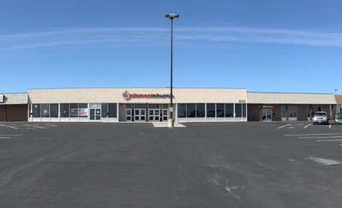 A large retail building with a parking lot, featuring a sign for "humanitarian" and clear blue skies.