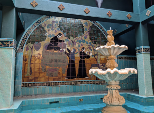 A decorative mural featuring figures and a fountain in a turquoise tiled space.