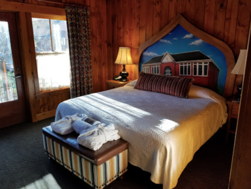 Cozy wooden bedroom with a large bed, decorative headboard, and natural light from a window. Towels are neatly arranged.