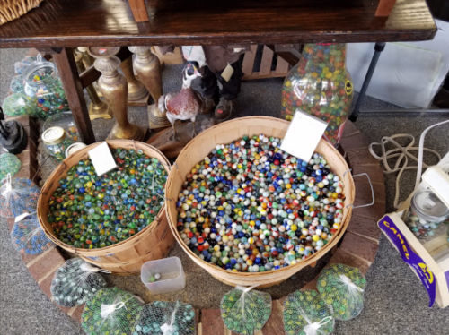 Two baskets filled with colorful marbles, surrounded by various glass jars and decorative items in a vintage shop.