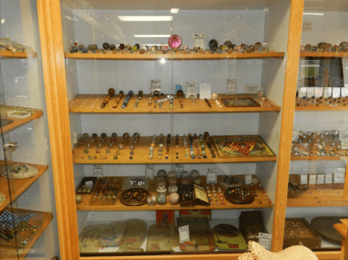 A display case filled with various colorful marbles and glass objects arranged on wooden shelves.