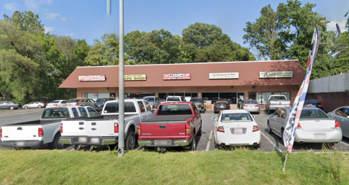 A parking lot with several vehicles in front of a strip mall featuring various shops and businesses.