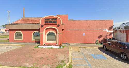 Exterior of a red building with a curved entrance, labeled "BBQ," surrounded by a parking lot and clear blue sky.