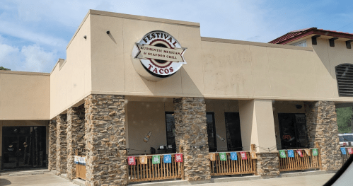 Exterior of Festival Tacos restaurant featuring a stone facade and colorful banners, with an "Open" sign visible.
