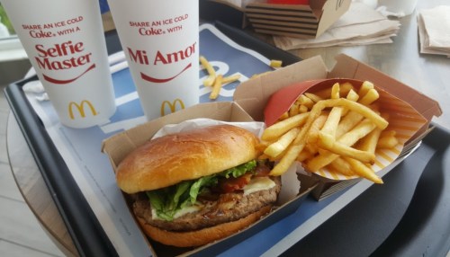 A McDonald's meal featuring a burger with lettuce and tomato, a side of fries, and two soft drink cups.