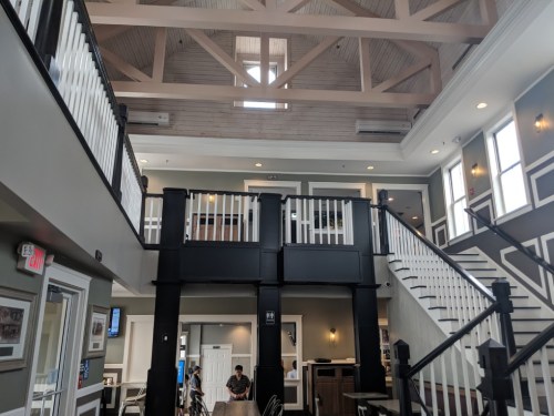 Interior of a spacious building with high ceilings, wooden beams, and a staircase, featuring a modern design.