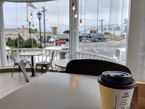 A coffee cup on a table with a view of a street and cloudy sky through large windows.