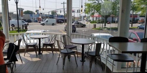 A bright café interior with empty tables and chairs, overlooking a busy street with vehicles and shops outside.