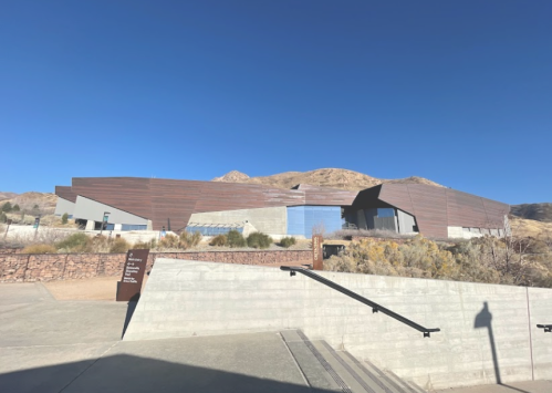 Modern building with angular design, surrounded by arid landscape and mountains under a clear blue sky.