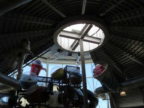 View of a circular skylight surrounded by whimsical sculptures of food and drinks hanging from the ceiling.