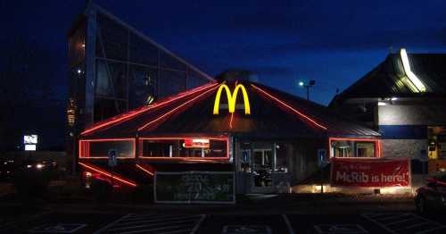 A McDonald's restaurant illuminated at night, featuring bright red lights and a prominent golden arch logo.