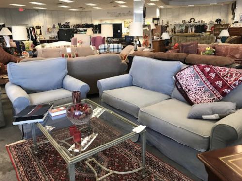 A cozy furniture store display featuring two gray sofas, a glass coffee table, and decorative items on a rug.