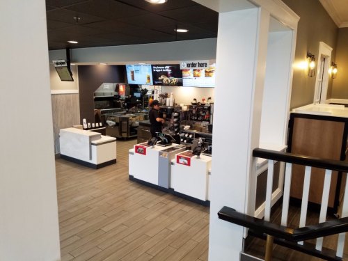 A view of a fast-food restaurant interior with a counter, menu screens, and a staff member preparing orders.