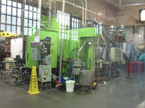 Industrial machinery in a factory setting, featuring green tanks and various pipes, with safety signage visible.