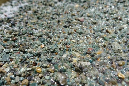 Close-up of a textured surface covered in small, colorful pebbles and wet sand, glistening in the light.