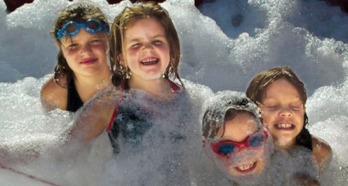Four children play joyfully in a bubbly pool, smiling and enjoying the fun.