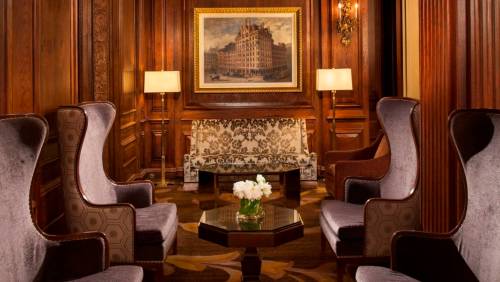 Elegant lounge with wooden walls, plush chairs, a floral sofa, and a painting, creating a cozy atmosphere.