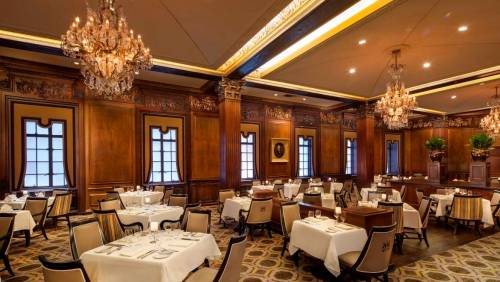 Elegant restaurant interior with wooden walls, chandeliers, and neatly set tables.
