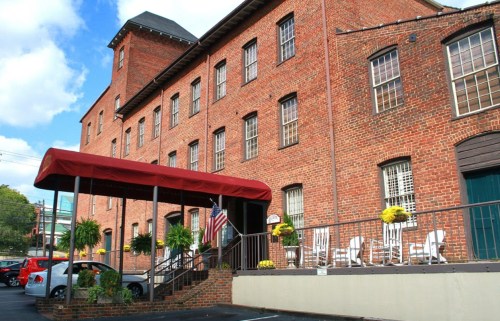 A brick building with a red awning, potted plants, and rocking chairs on the porch, set against a blue sky.