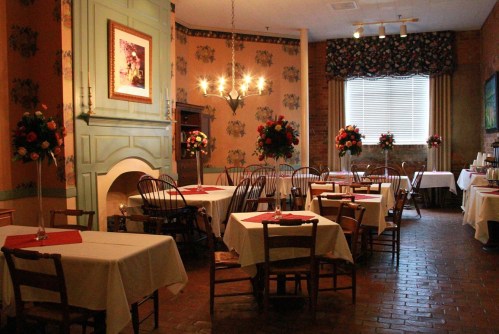 Cozy restaurant interior with tables set for dining, floral decorations, and warm lighting.