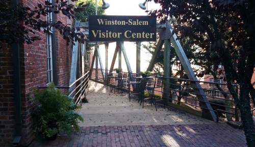 A pathway leading to the Winston-Salem Visitor Center, surrounded by greenery and brick buildings.