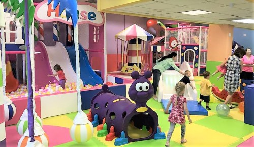 Colorful indoor play area with slides, ball pit, and children playing on various structures and toys.