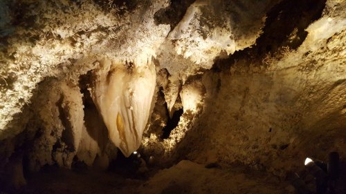 A dimly lit cave interior featuring stalactites and stalagmites, with rocky walls and a natural, rugged texture.