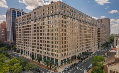 A large, historic building with a brick facade, surrounded by trees and city streets under a partly cloudy sky.