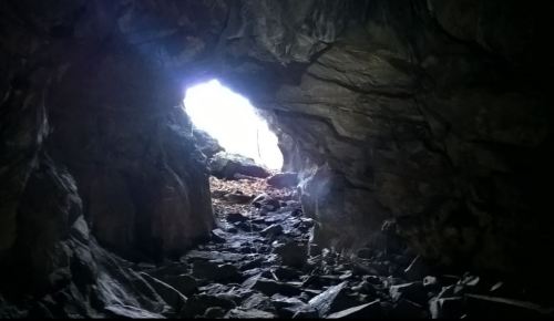 A view from inside a cave, showing a bright light at the entrance and rocky terrain scattered with stones.