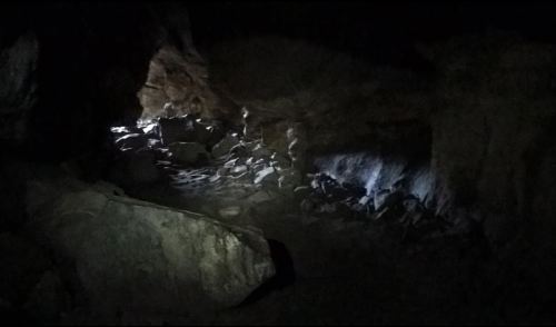 A dimly lit cave interior with scattered rocks and a faint light illuminating part of the space.