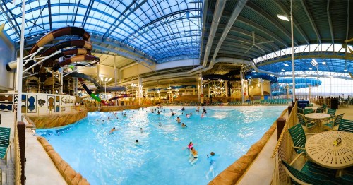 Indoor water park featuring a large wave pool, water slides, and numerous visitors enjoying the water.