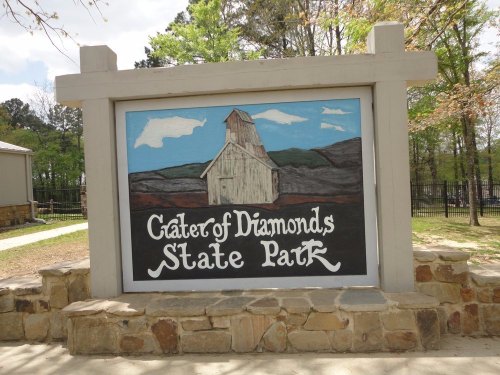 Sign for Crater of Diamonds State Park featuring a painted old building and scenic background.
