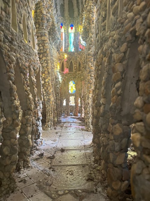 A stone corridor with colorful stained glass windows, featuring textured walls and a sandy floor.