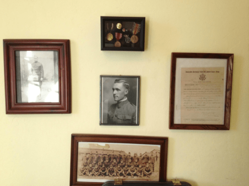 A wall display featuring framed photos, medals, and a certificate, honoring military service and history.