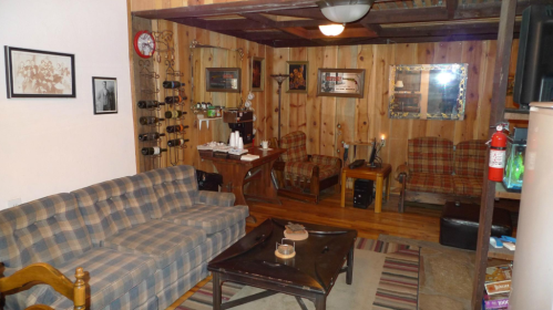 Cozy living room with wooden walls, plaid furniture, a coffee table, and decorative items on shelves.