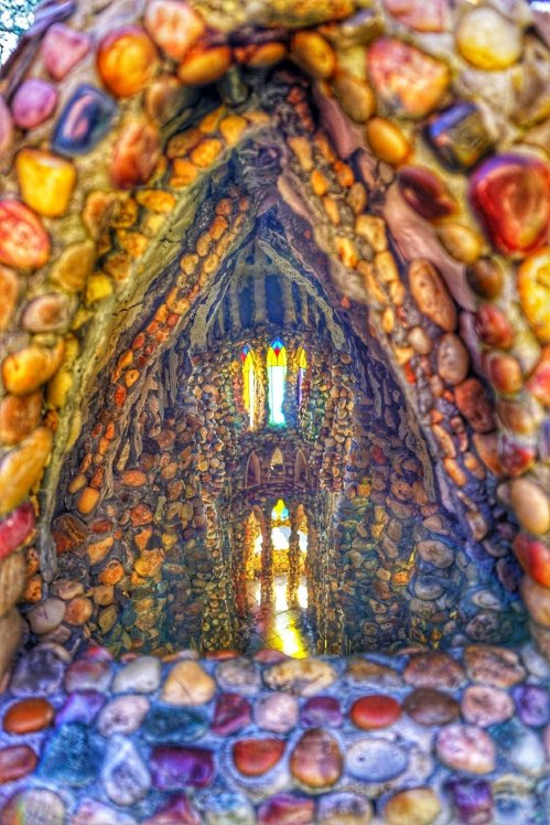 Colorful stone interior of a unique, artistic structure with stained glass windows and intricate designs.