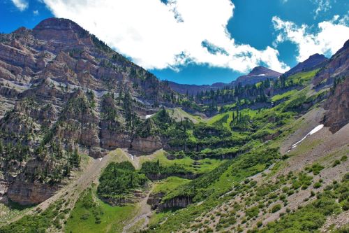 Lush green mountains with rocky cliffs under a bright blue sky and scattered clouds.