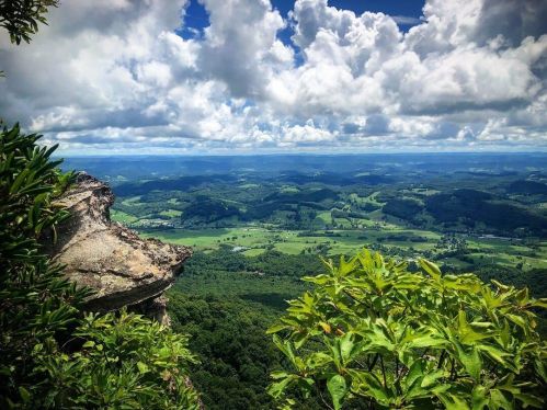 A panoramic view of lush green hills and valleys under a dramatic sky filled with clouds.