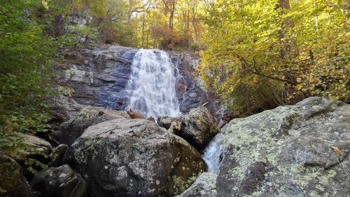 A serene waterfall cascades over rocky terrain, surrounded by vibrant autumn foliage.