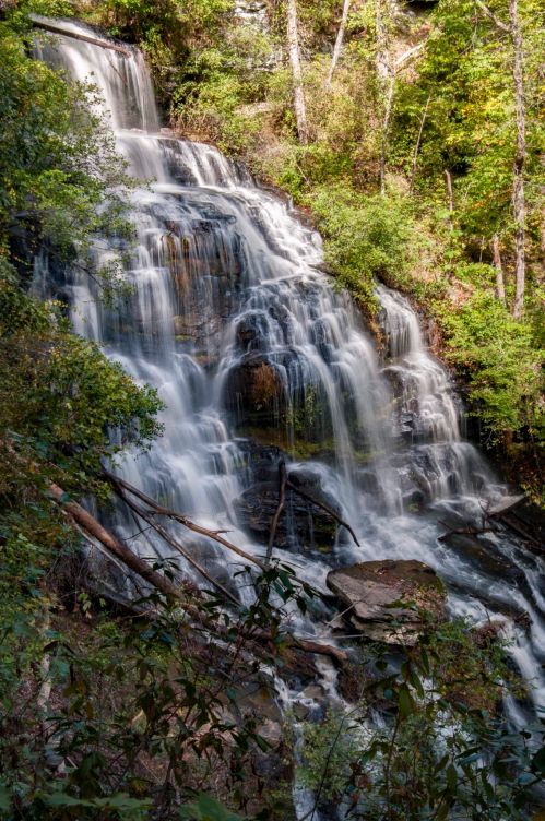 A cascading waterfall surrounded by lush greenery and rocky terrain, creating a serene natural scene.
