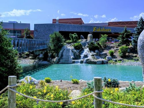 A scenic view of a pond with a waterfall, surrounded by greenery, in front of the Kalahari resort.