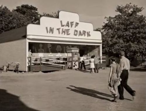 A vintage amusement attraction called "Laff in the Dark," with people walking by and trees in the background.