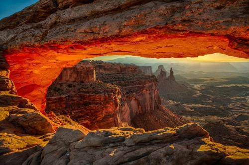 A stunning view of a rocky landscape framed by a glowing arch at sunset, highlighting the natural beauty of the area.