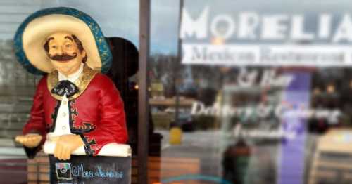 A colorful statue of a smiling man in traditional Mexican attire stands outside a restaurant, holding a sign.