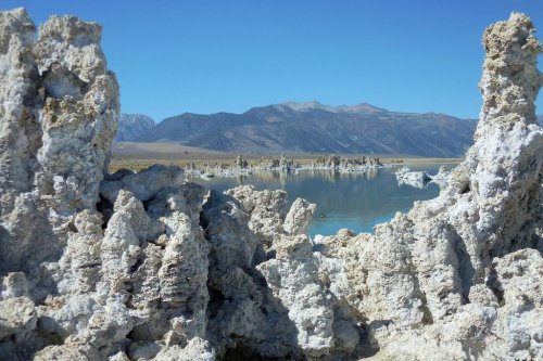 A scenic view of a lake surrounded by unique rock formations and mountains under a clear blue sky.