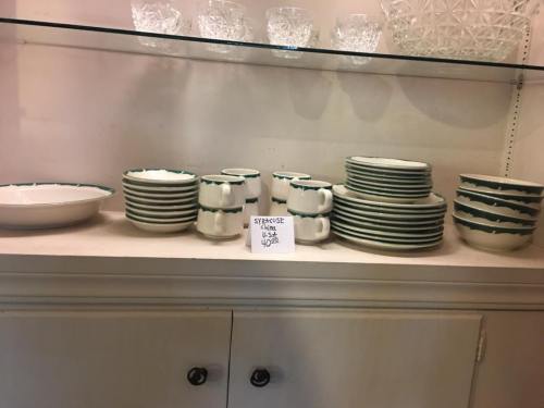 A shelf displaying various dishes, including plates, bowls, and mugs, with a sign labeled "Syracuse China."