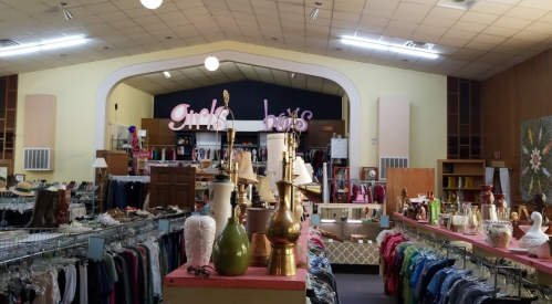 Interior of a thrift store with sections labeled "Girls" and "Boys," featuring clothing racks and various decor items.