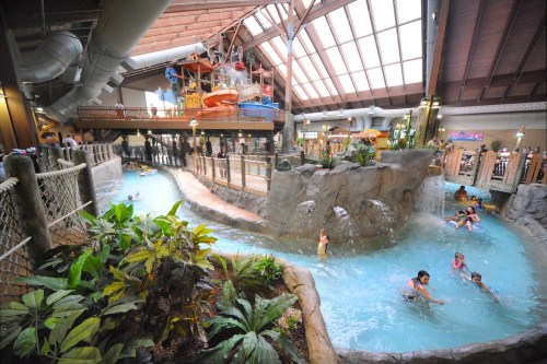 Indoor water park featuring a lazy river, water slides, and lush greenery, with families enjoying the water.