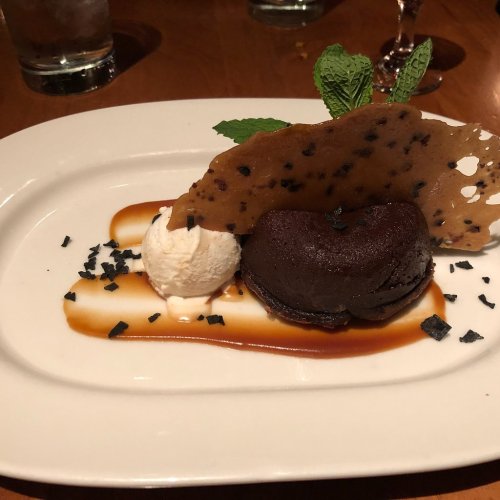A dessert plate featuring a chocolate fondant, vanilla ice cream, caramel sauce, and a crispy chocolate shard.