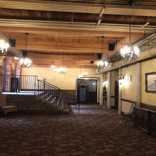 Interior of a spacious room with chandeliers, a staircase, and vintage decor, featuring warm lighting and a cozy atmosphere.